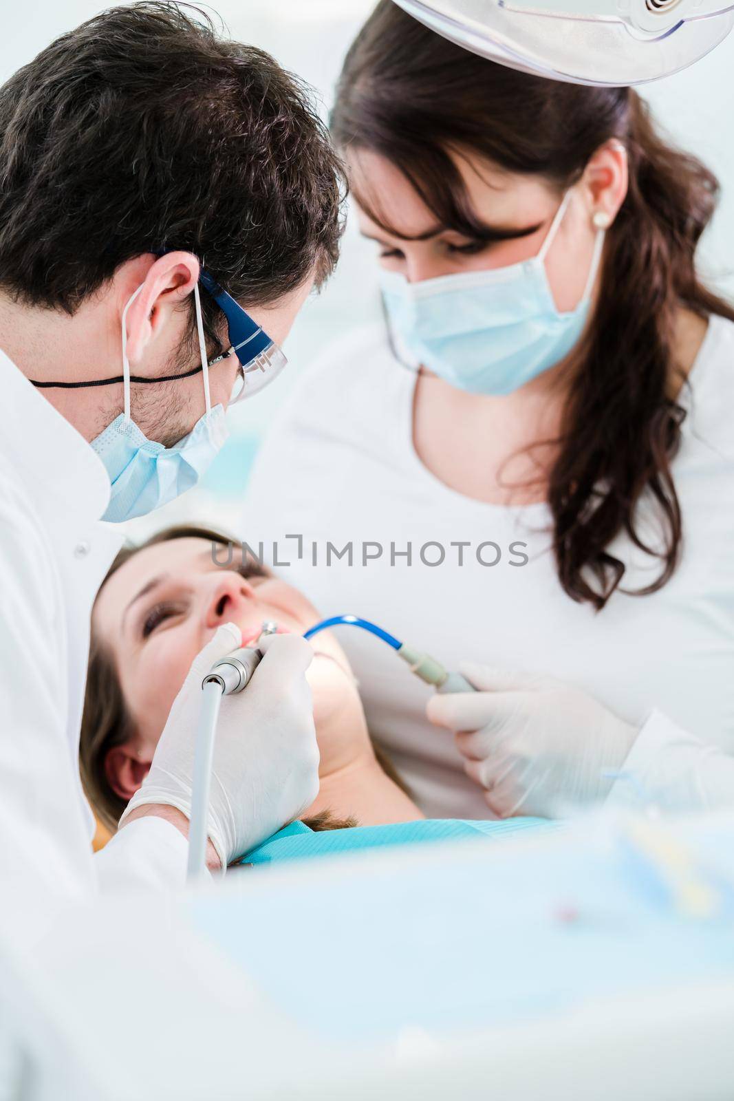 Dentist treating woman patient using drill on her teeth