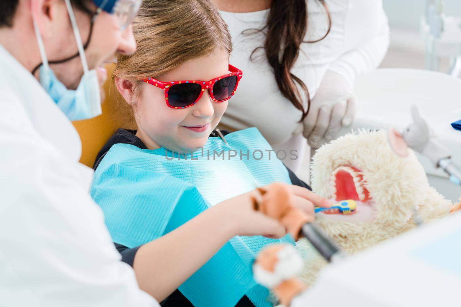 Child at dentist office looking after teeth of pet toy, the doctor relieving the kid of her fear that way