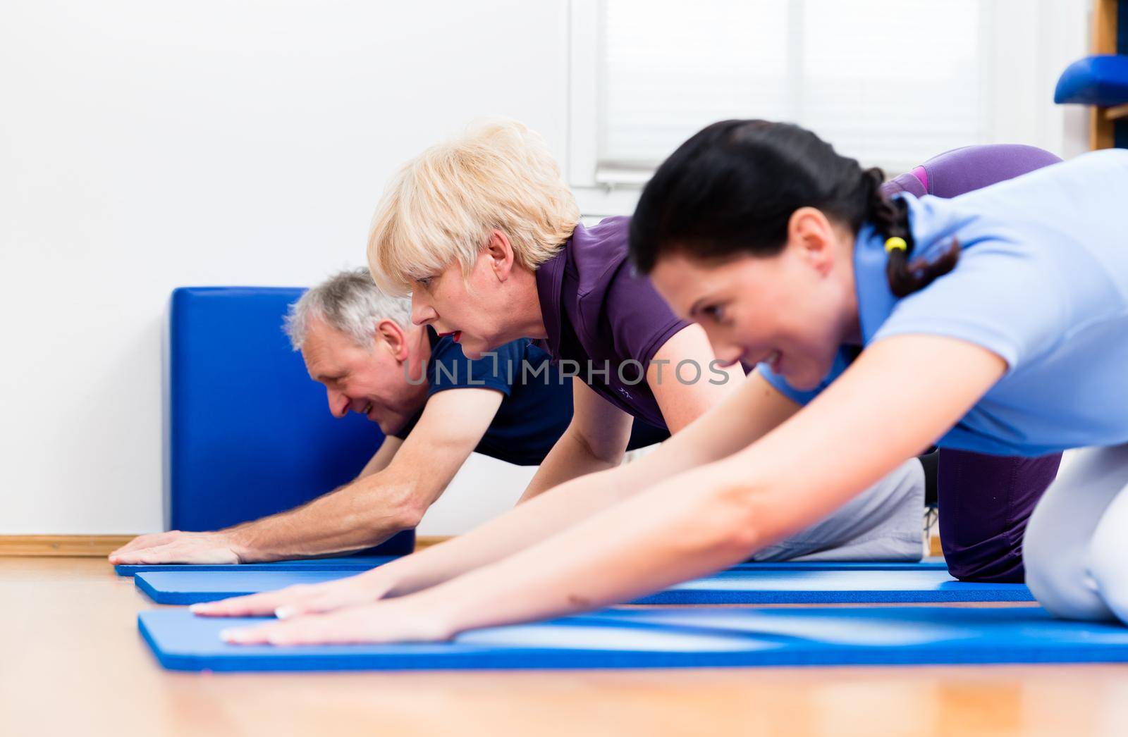 Senior woman and man doing floor gymnastics with physiotherapist