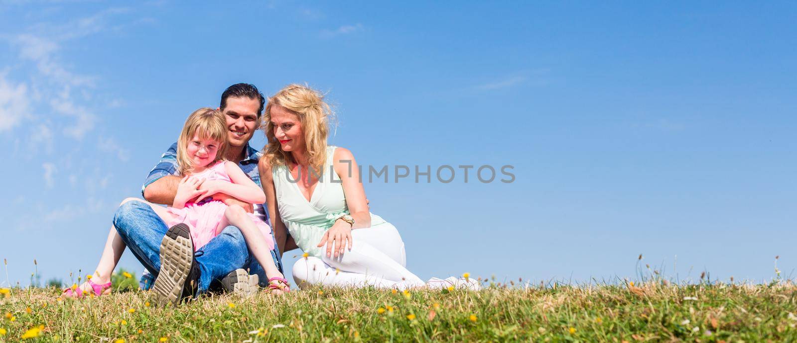 Girl on dads lap, Mom sitting next to them in field