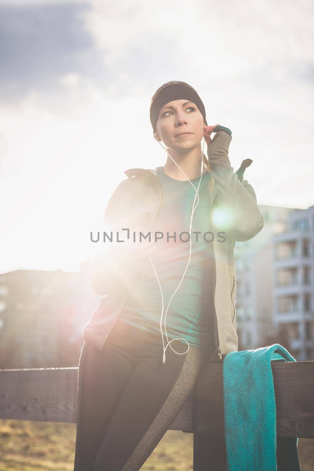 Portrait of young woman ready for outdoor workout listening to music through in-ear headphones connected to the mobile phone