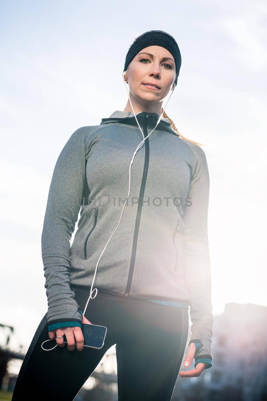 Beautiful thoughtful young woman listening to music on her mobile phone while wearing trendy sport outfits in a sunny day in the park