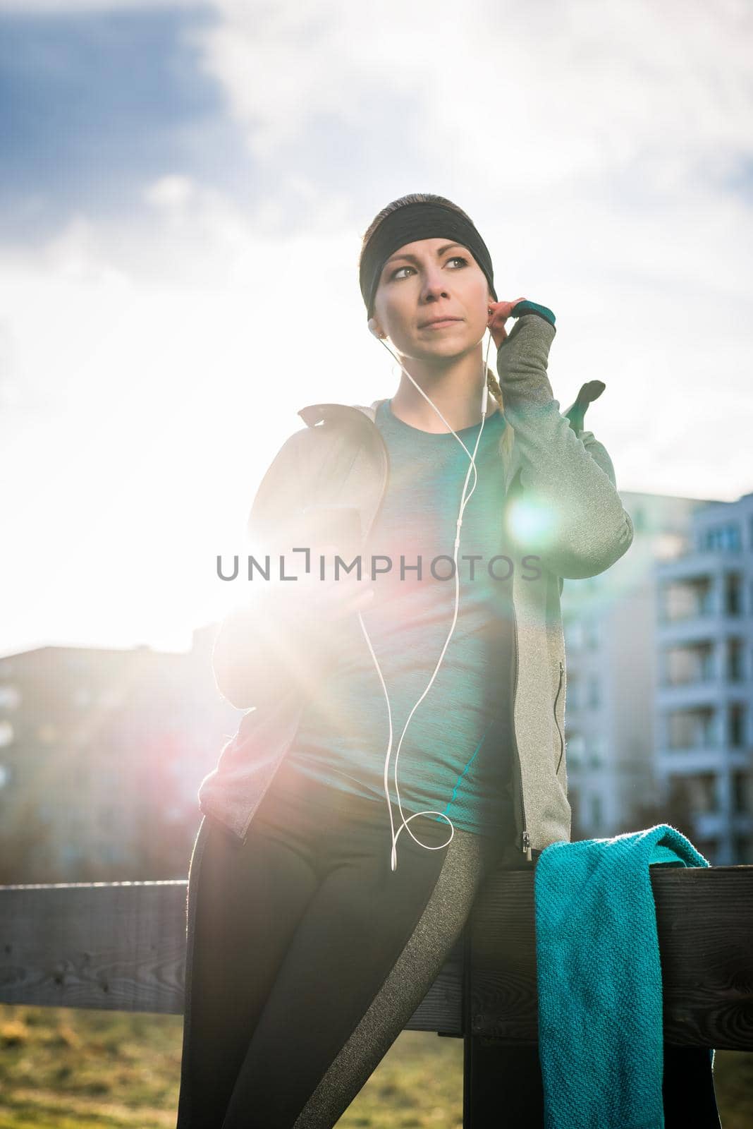 Portrait of young woman ready for outdoor workout listening to music through in-ear headphones connected to the mobile phone