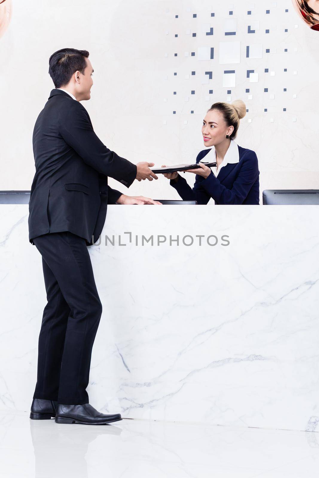 Job Applicant at business front desk giving his documents to receptionist