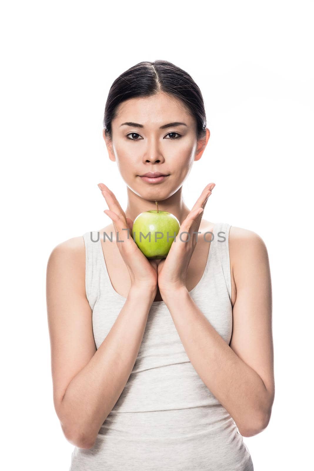 Thoughtful young Asian woman holding a green apple against white background