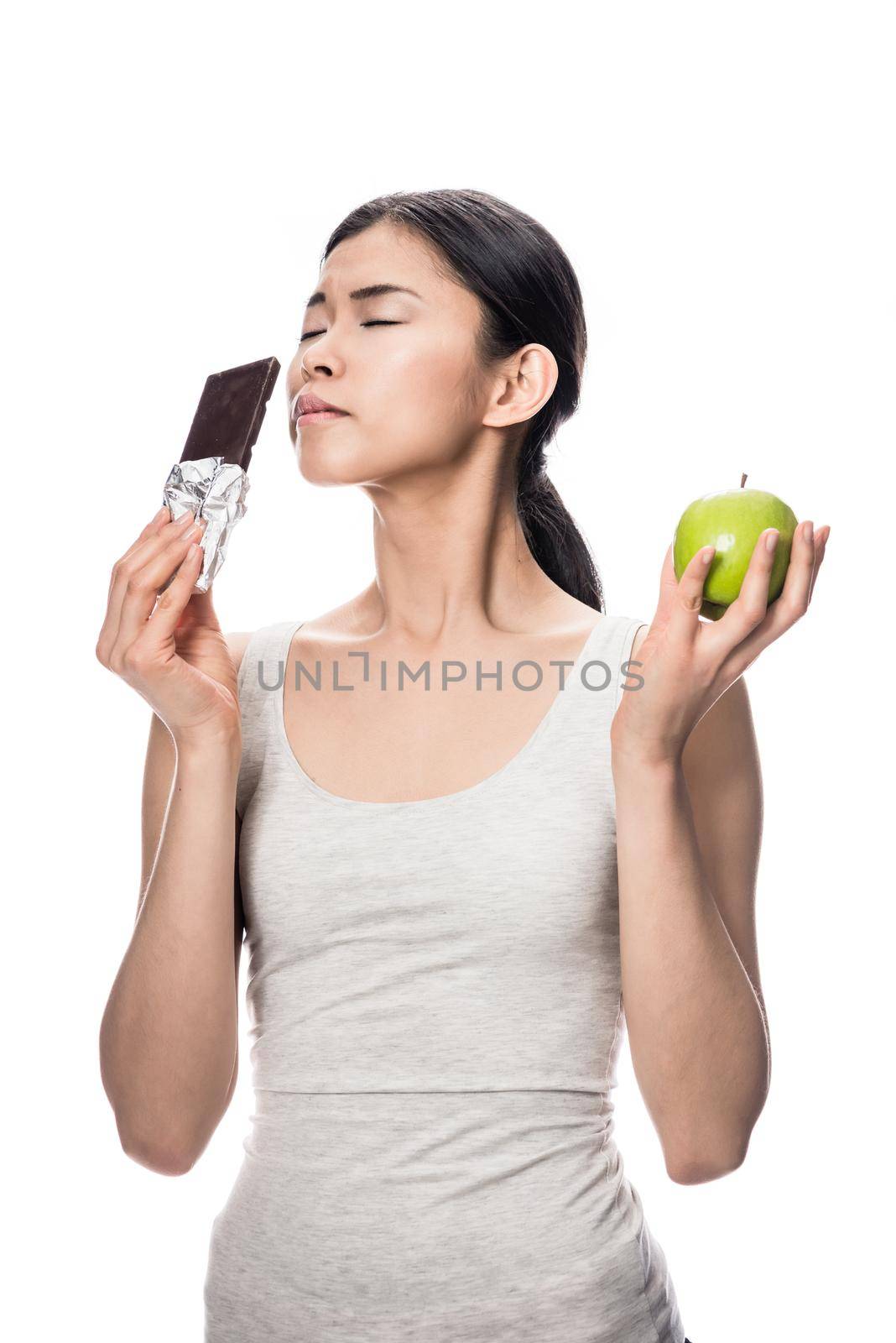 Funny young woman eating a fresh apple while looking at a chocolate bar