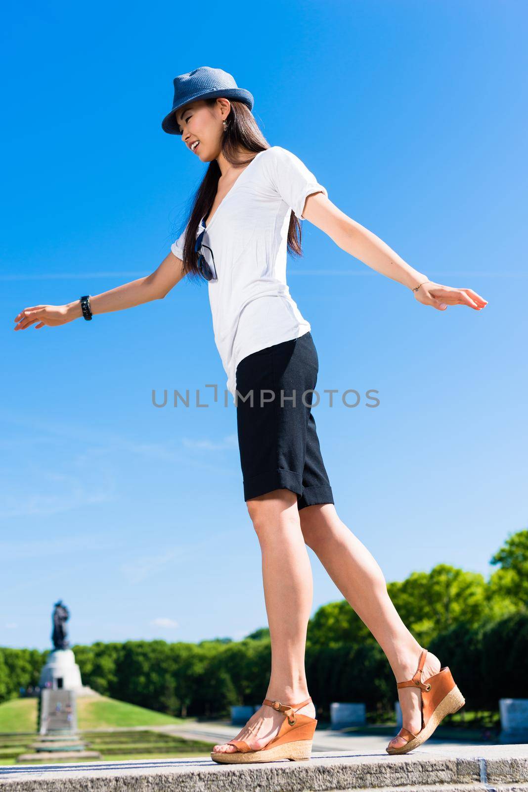 Low-angle view of young Asian woman standing on one leg outdoors in summer