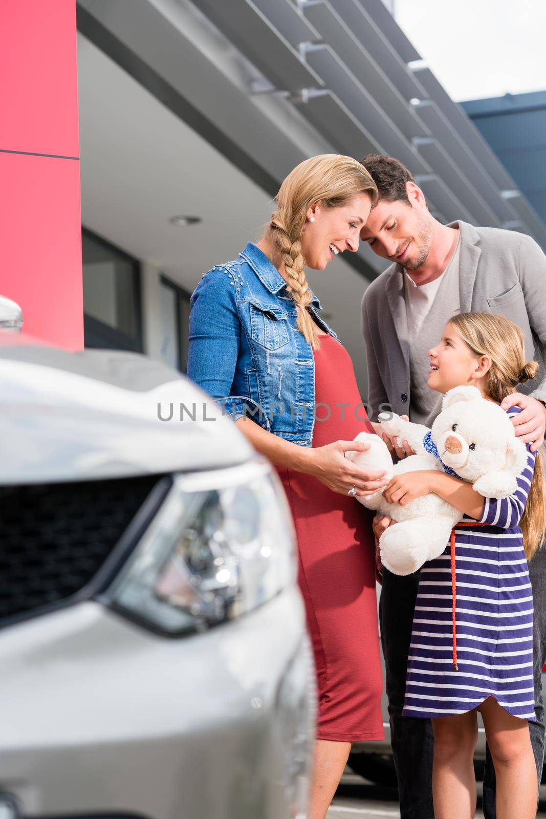 Mother, father, and child buying car at dealership by Kzenon