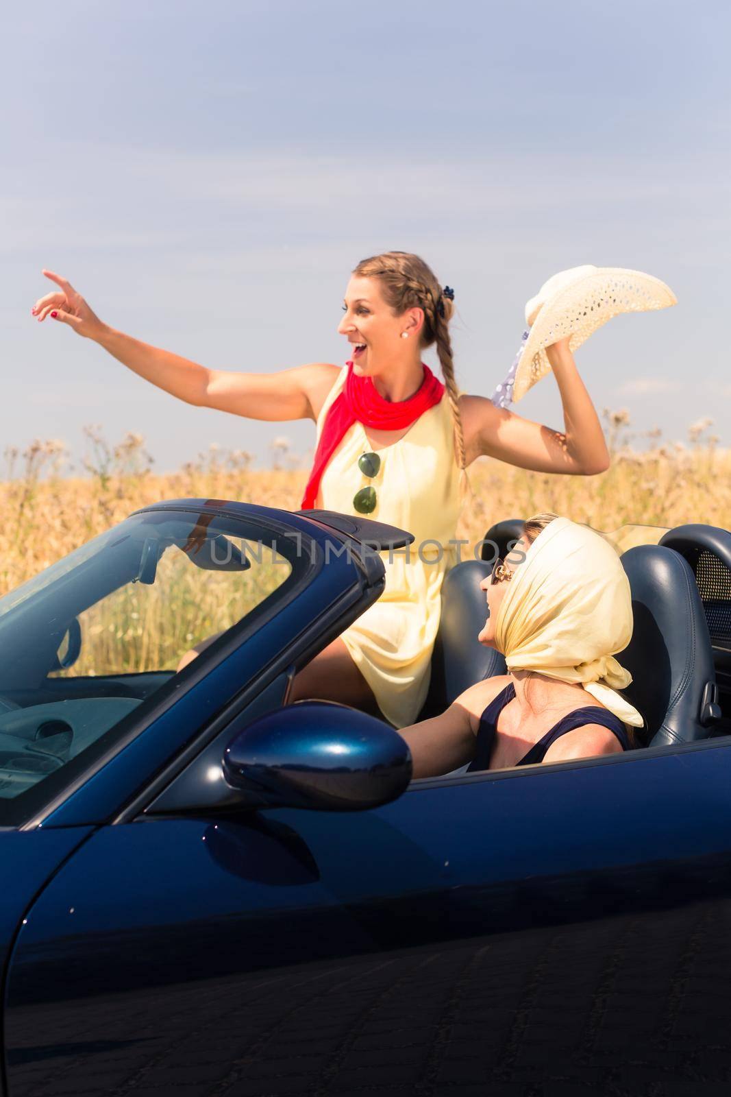 Best friends having summer joyride in convertible car passing a field