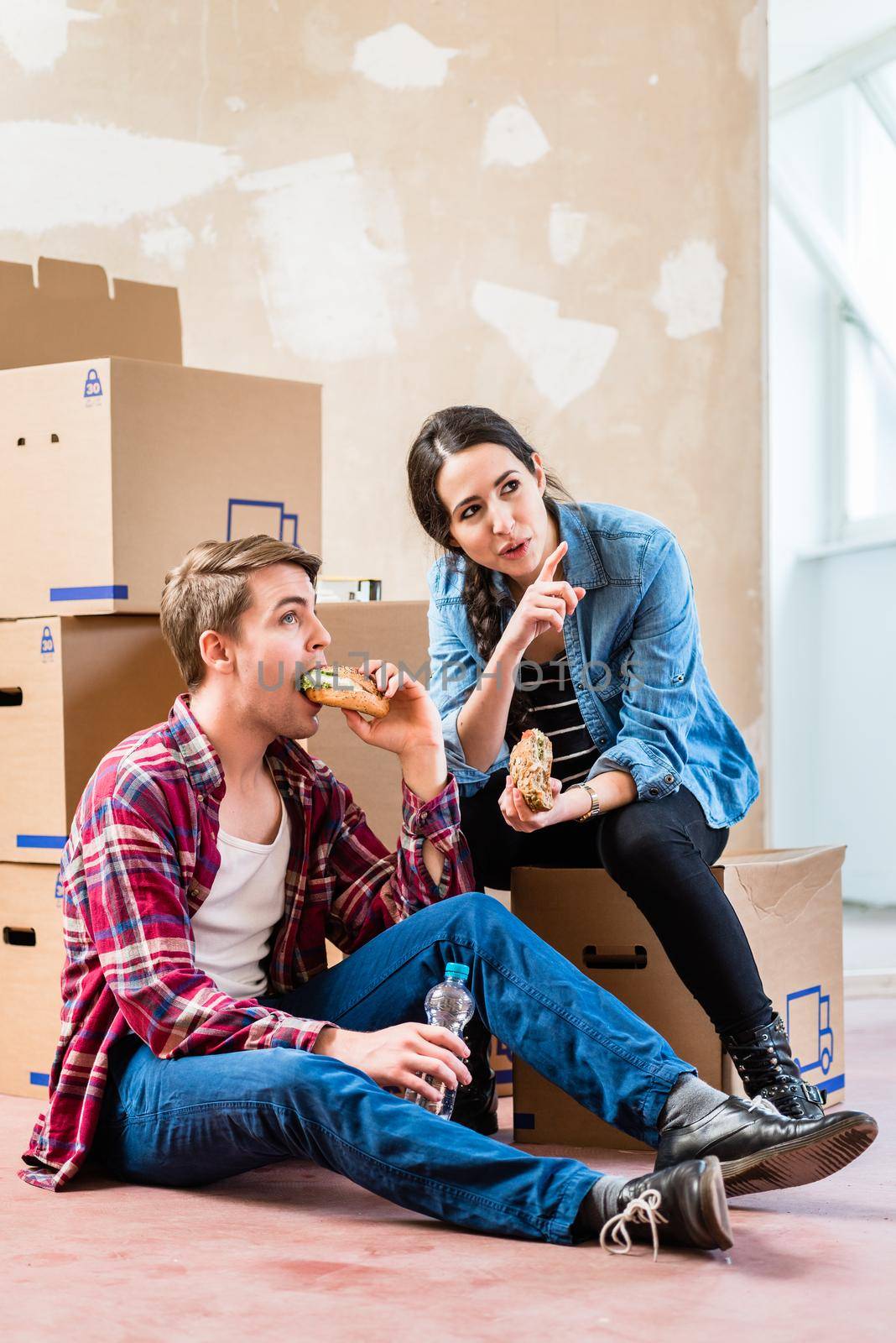 Young couple looking tired while eating a sandwich during break from renovation in the interior of their new home