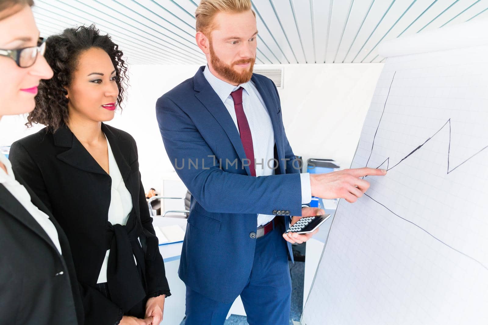 Business people analyze a graph on the whiteboard - man holds a pocket calculator and is pointing at the graph