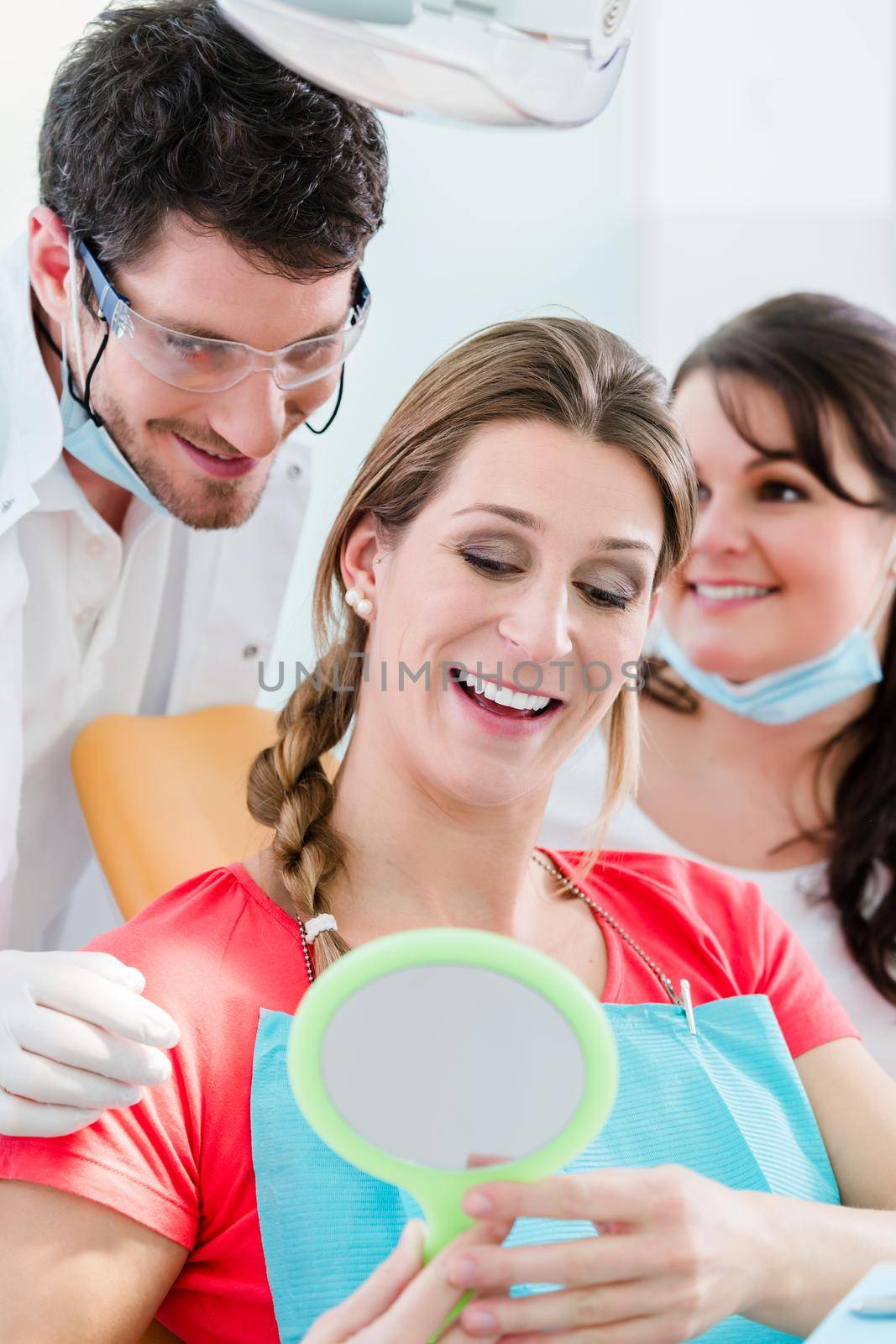 Woman after dental bleaching at dentist checking teeth in mirror