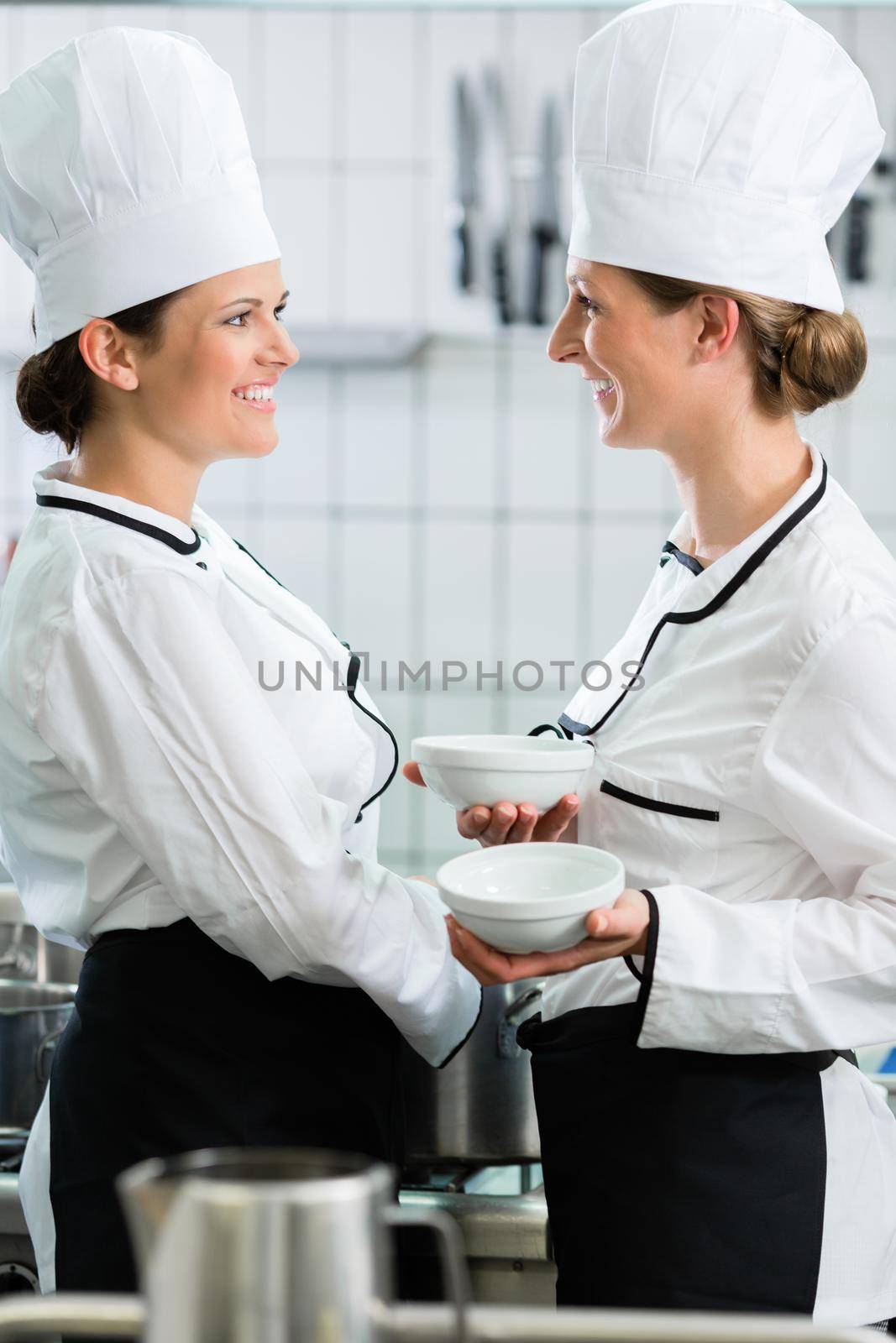 Two female chefs in gastronomic kitchen wearing white cooking uniforms