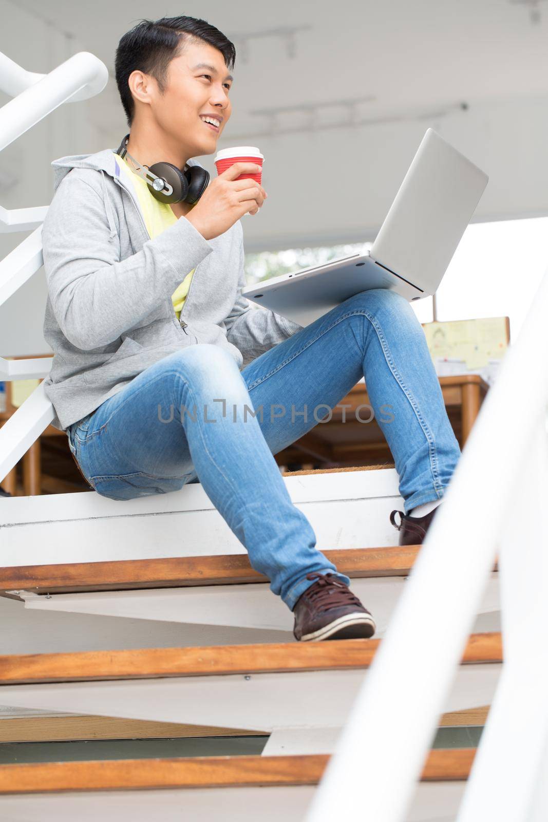 Happy young Asian employee using a laptop in a modern office by Kzenon