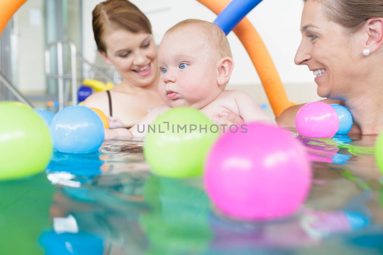 Mothers and their kids having fun at baby swimming lesson between lots of water balls