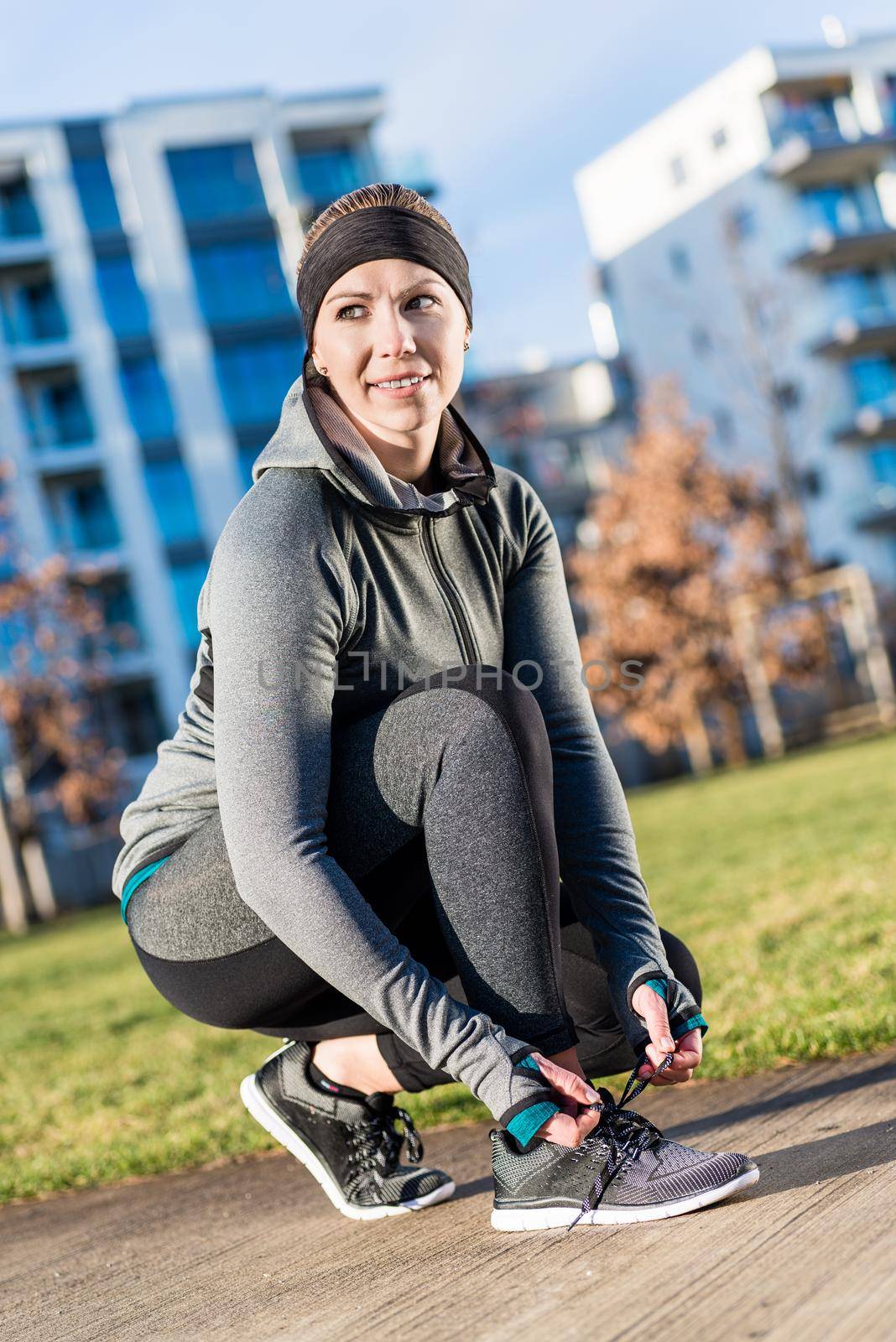 Full length of an active young woman tying the shoelaces of her sport shoes, while wearing trendy workout outfit in a sunny day in the park