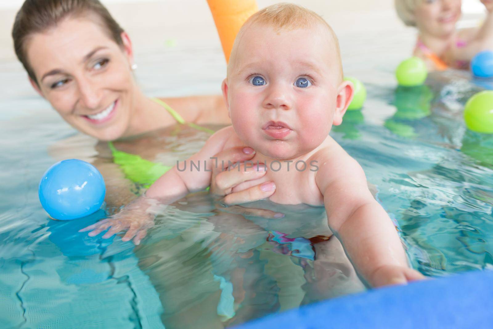 Mothers and their kids having fun at baby swimming lesson between lots of water balls