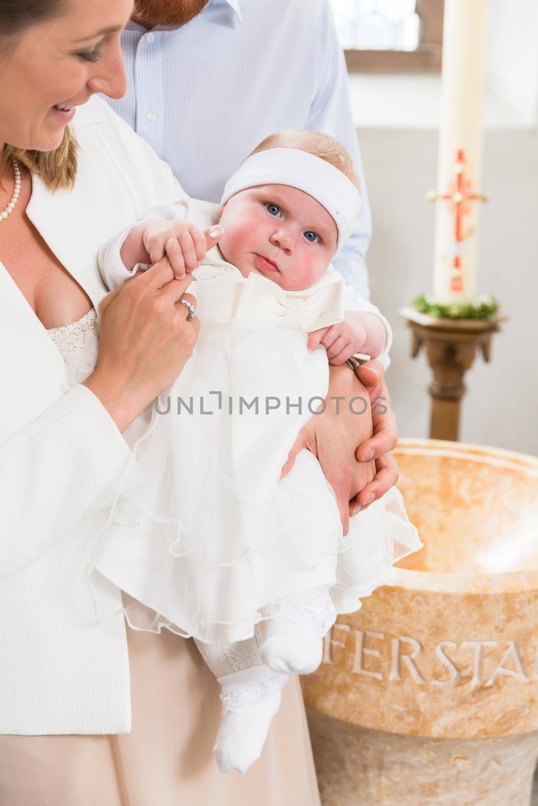 Young parents at the church with their baby wearing a christening gown