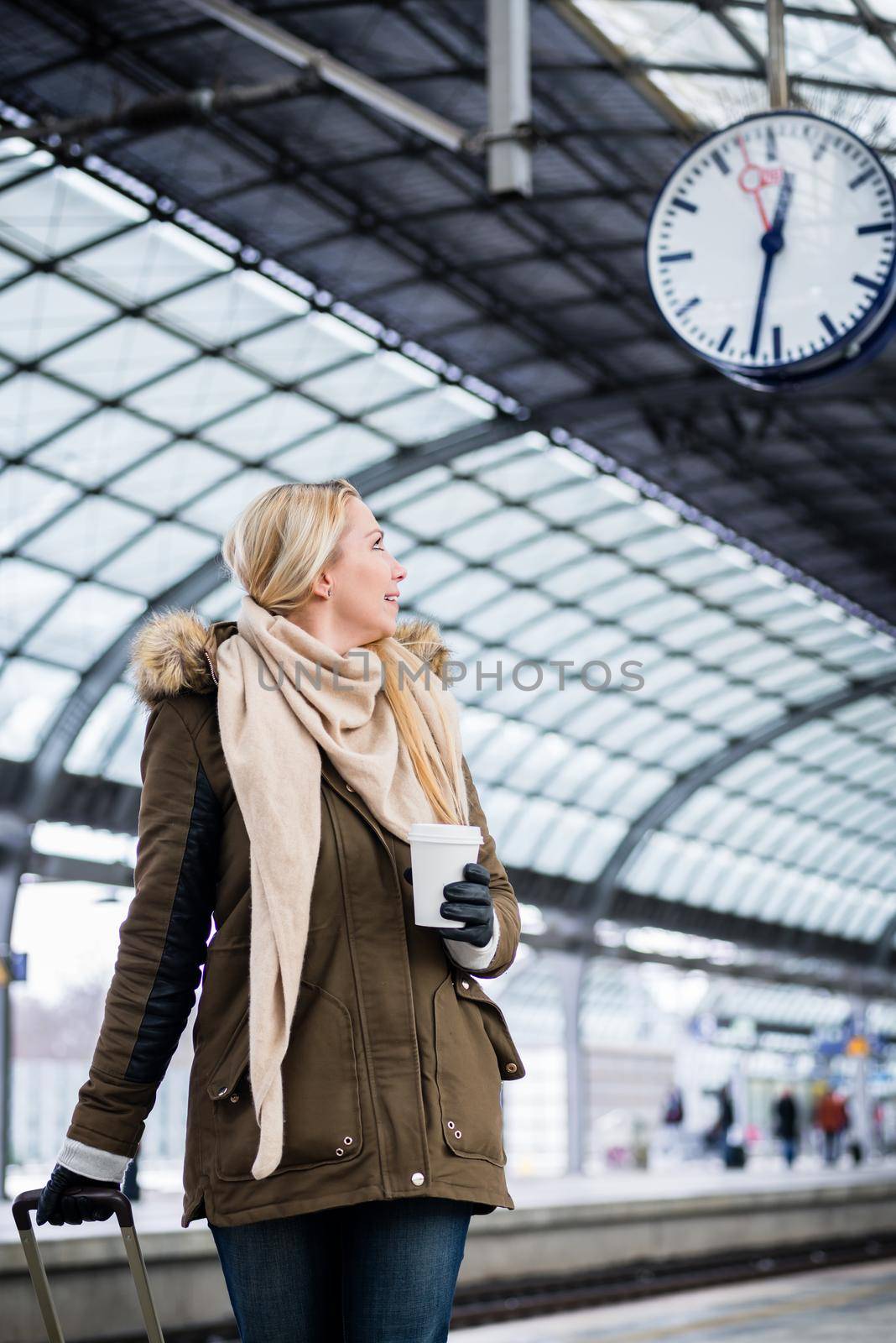 Woman looking impassionate at clock in train station as her train has a delay