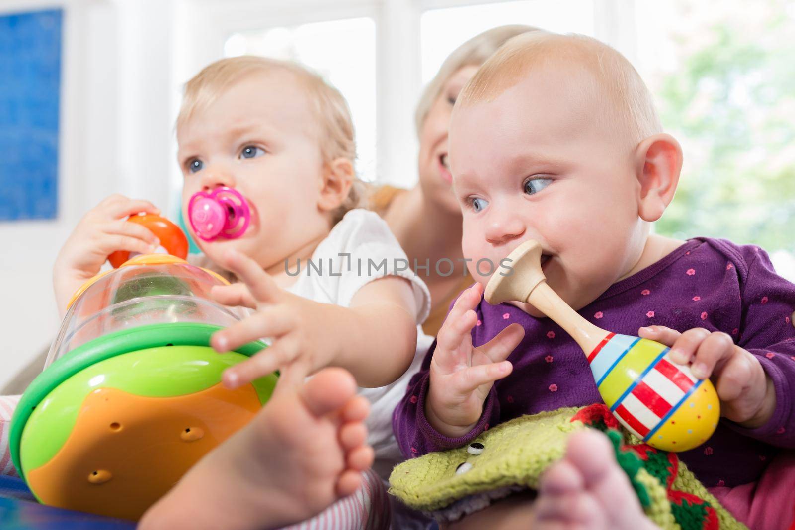 Babies with pacifier in toddler group playing with toys by Kzenon