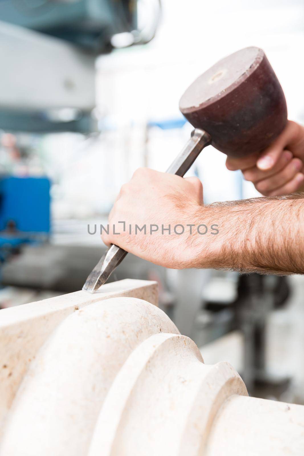 Stone carver working with hammer and chisel at marble column