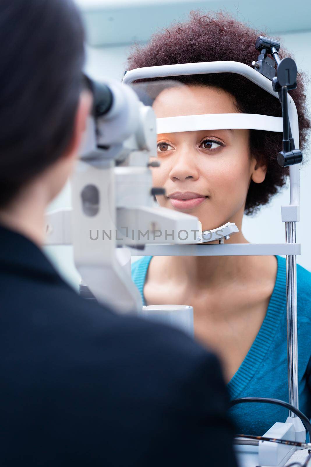 Optician measuring women eyes with refractometer by Kzenon