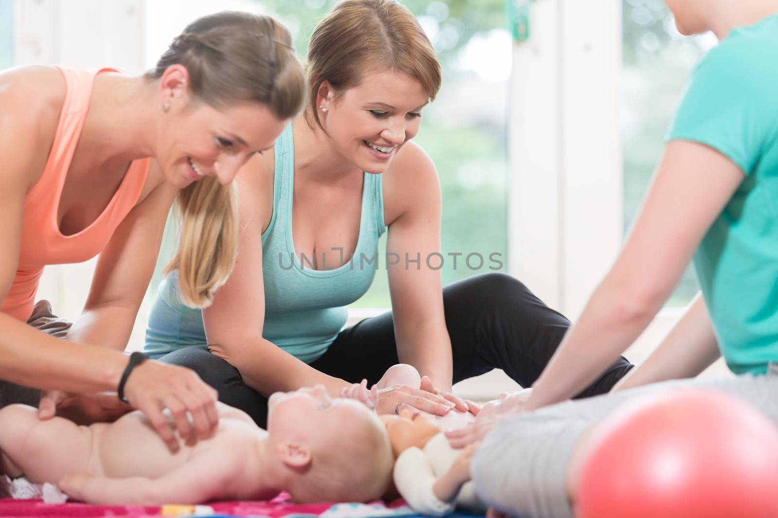 Young women practicing how to wrap children in mother-child lesson by Kzenon