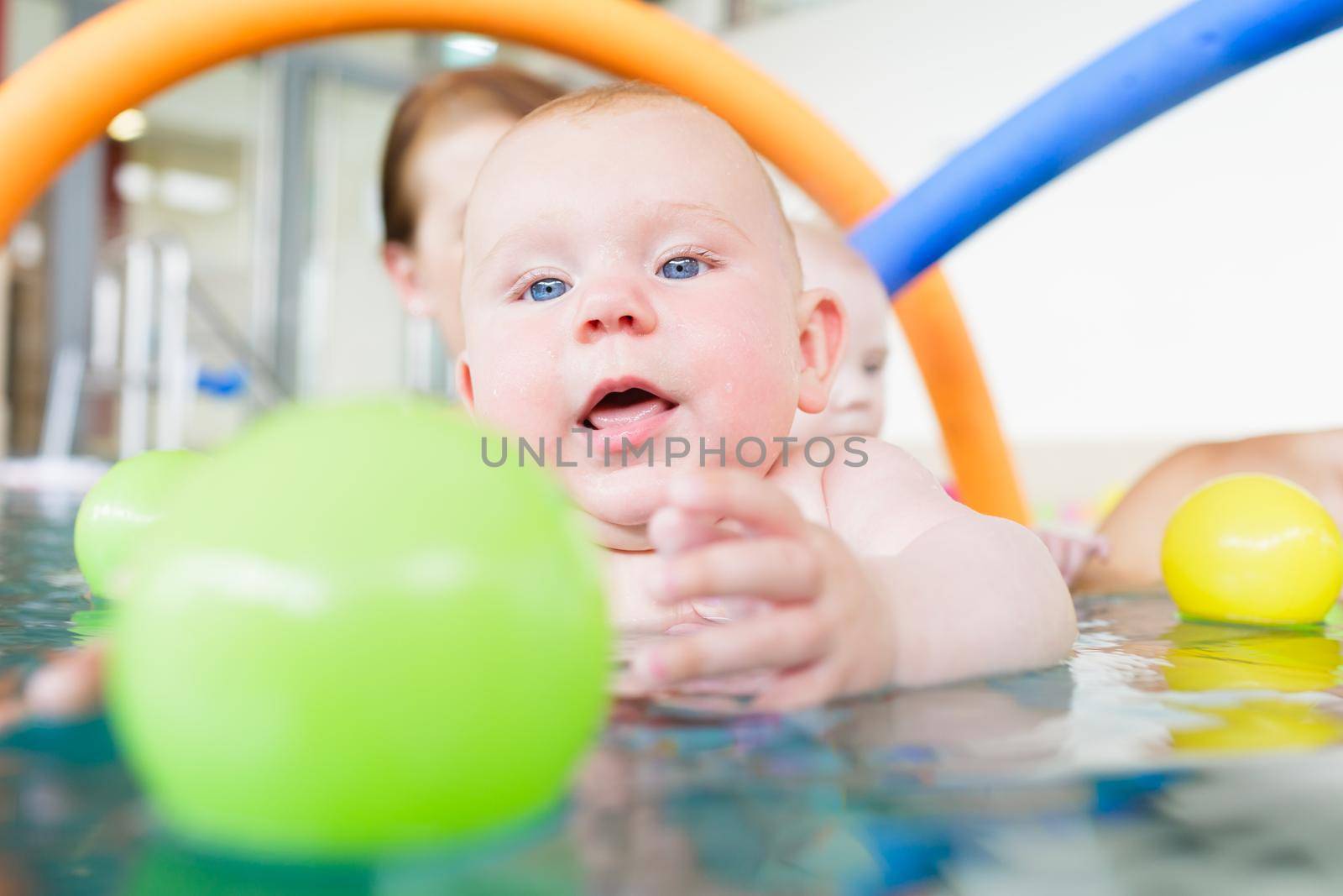 Baby in paddle pond reaching for toy ball in water by Kzenon