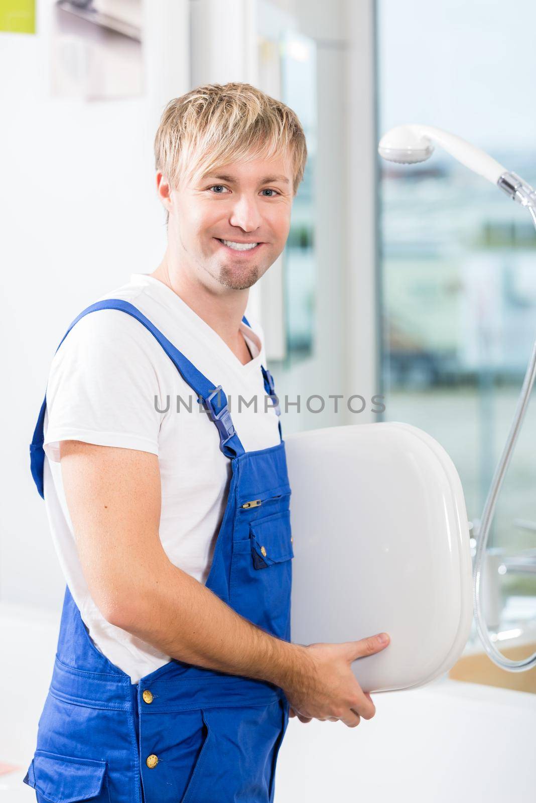 Portrait of a cheerful man wearing blue overall while working in a sanitary ware shop with modern fixtures and accessories for sale