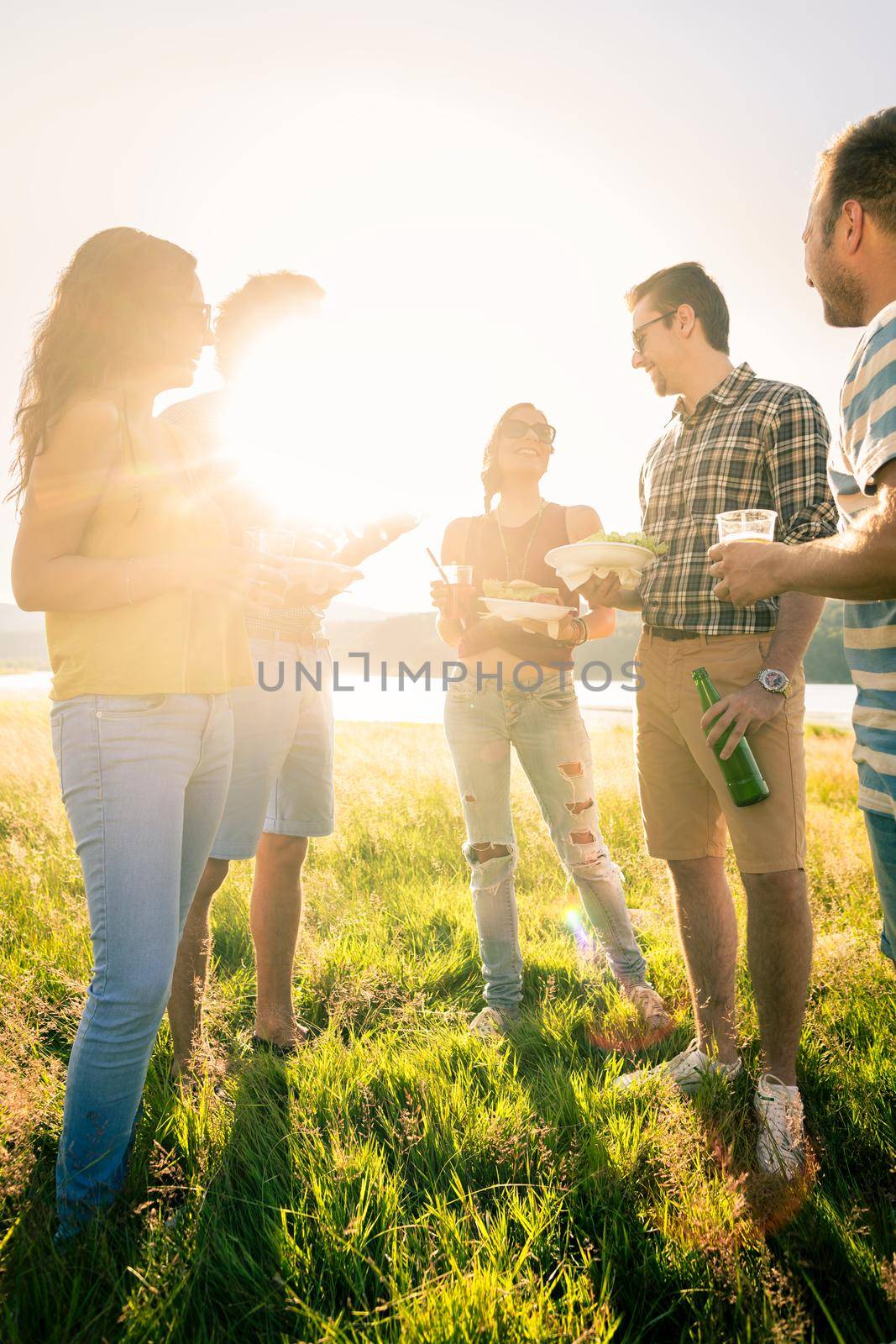 Circle of friends on summer BBQ party at lakeside having burgers and beer