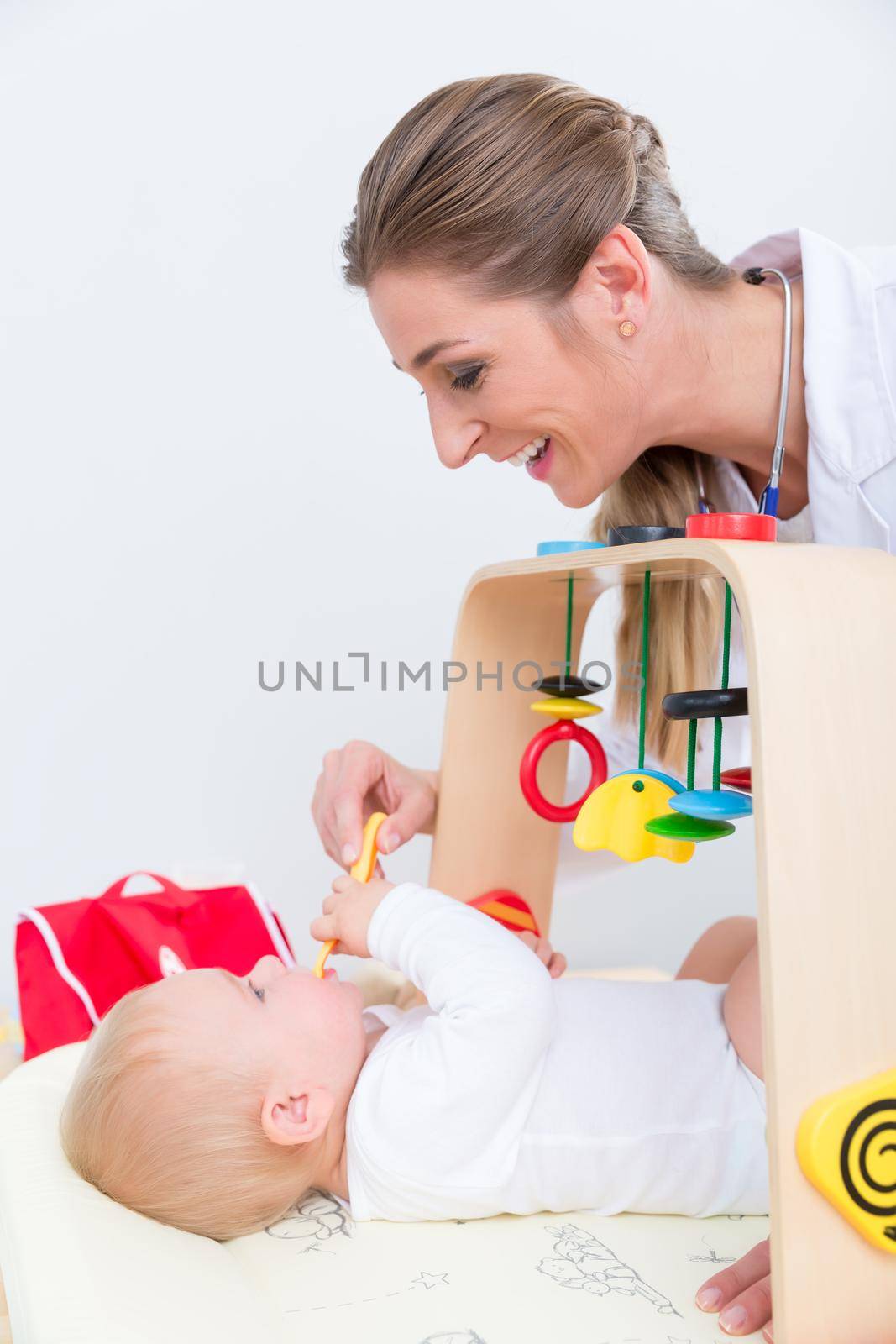 Dedicated female pediatrician smiling while playing with a healthy and active baby during physical exam in a modern medical center for children