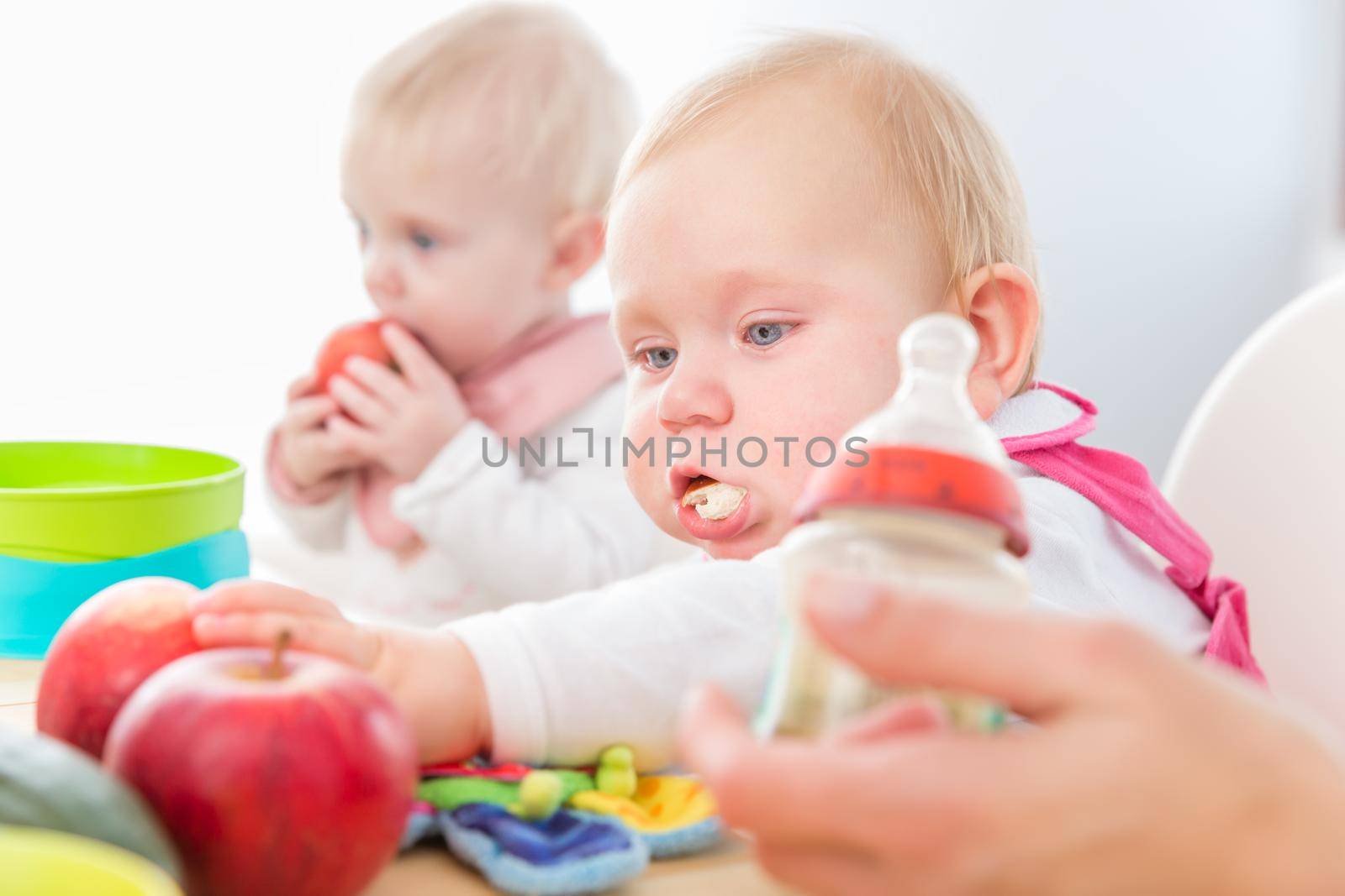 Cute baby girl eating healthy solid food in a modern daycare center by Kzenon