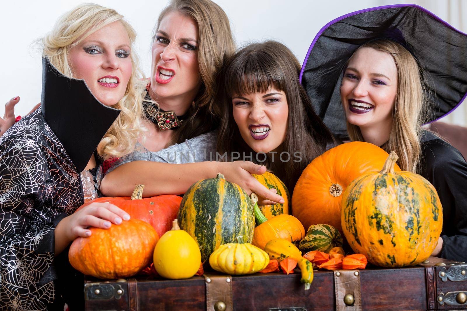 Four cheerful beautiful women toasting while celebrating Halloween together during costume party indoors in a decorated room