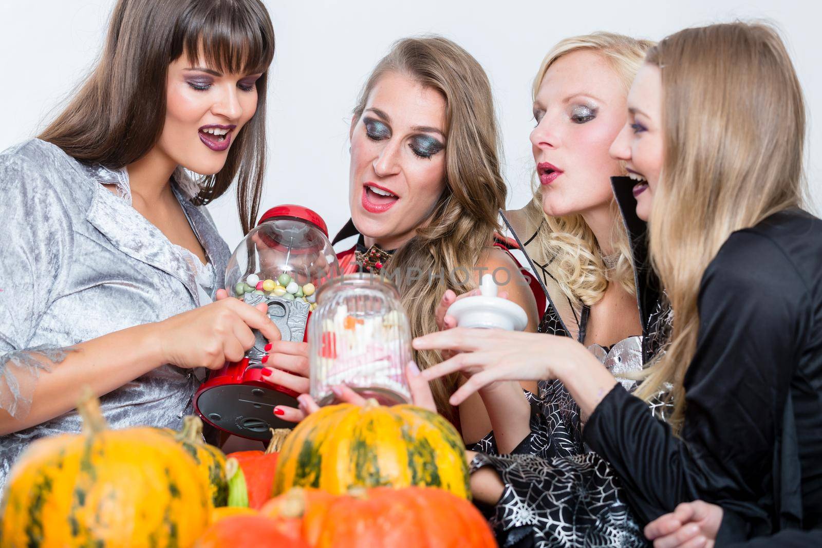 Funny young women and best friends sharing various delicious candies while celebrating Halloween together at costume party indoors