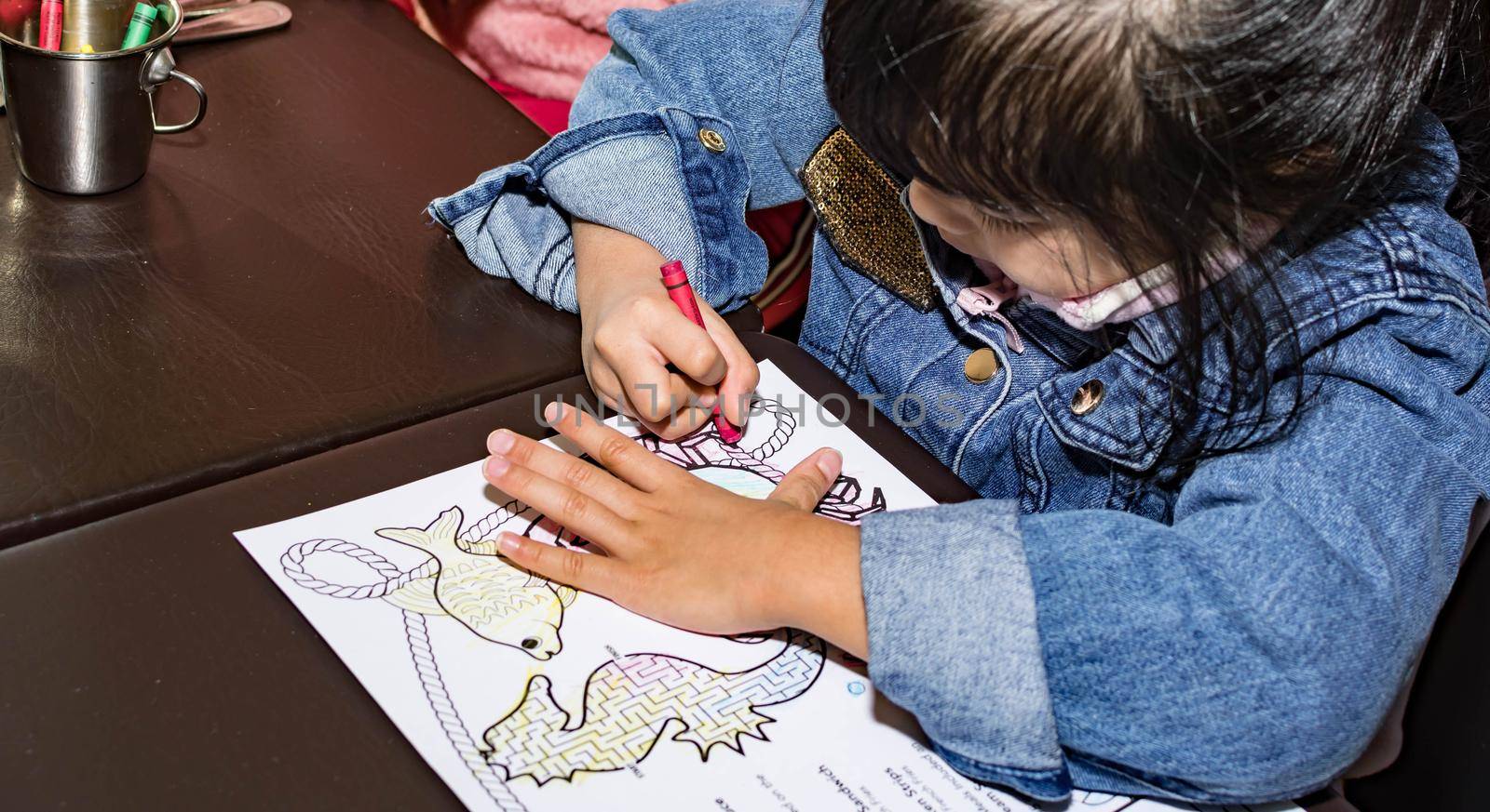 Pretty asian child right handed while doing a coloring activity with crayon and coloring book