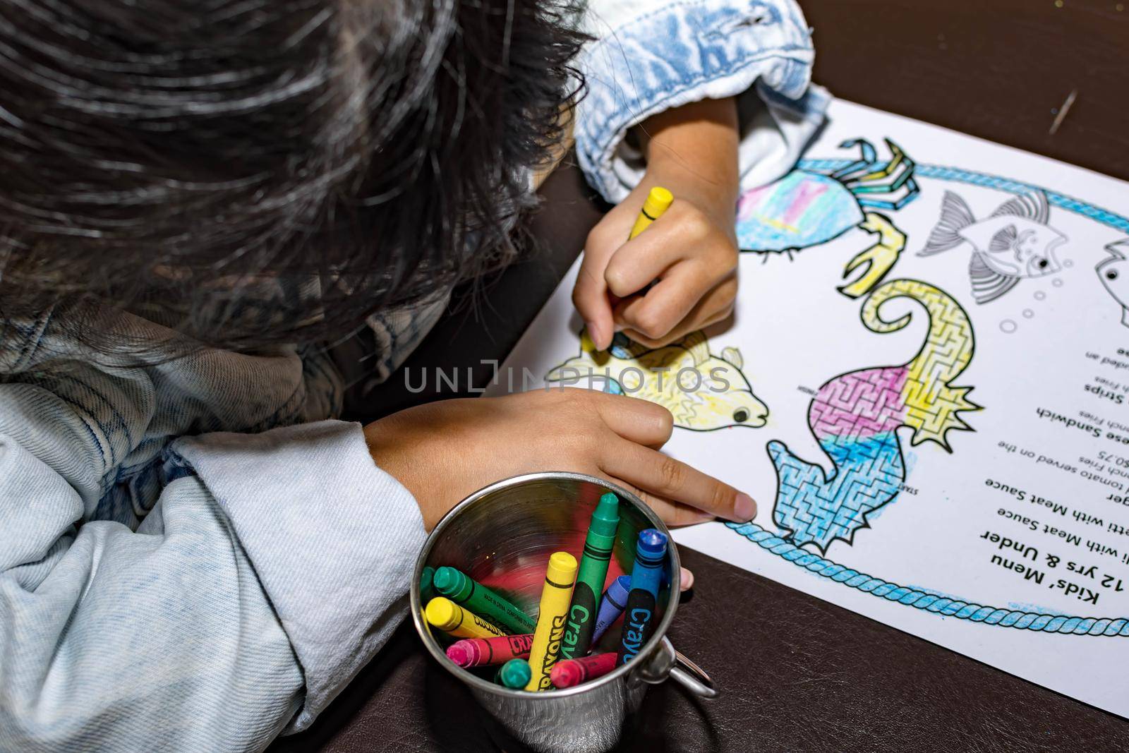 Pretty asian child left handed while doing a coloring activity with crayon and coloring book