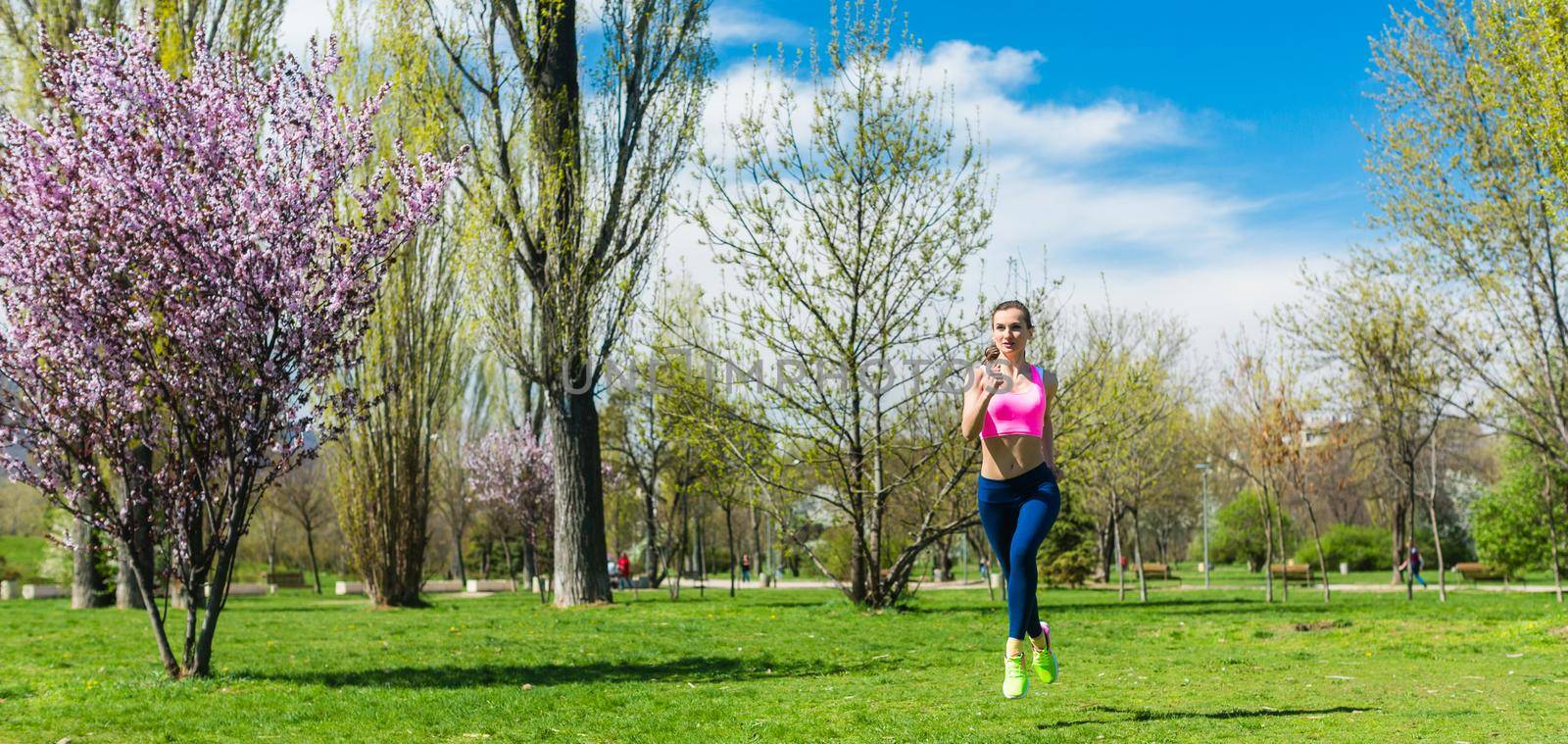Woman running for better fitness though a park in spring by Kzenon