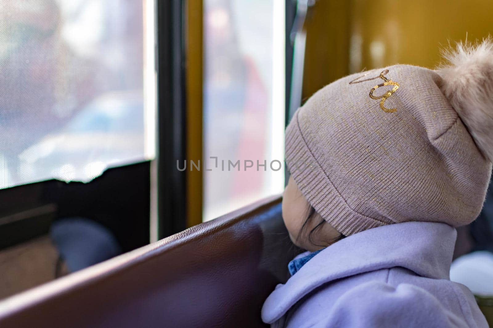 cute female child wearing purple coat and cute bonnet while sitting inside a bus and enjoying the view from the window