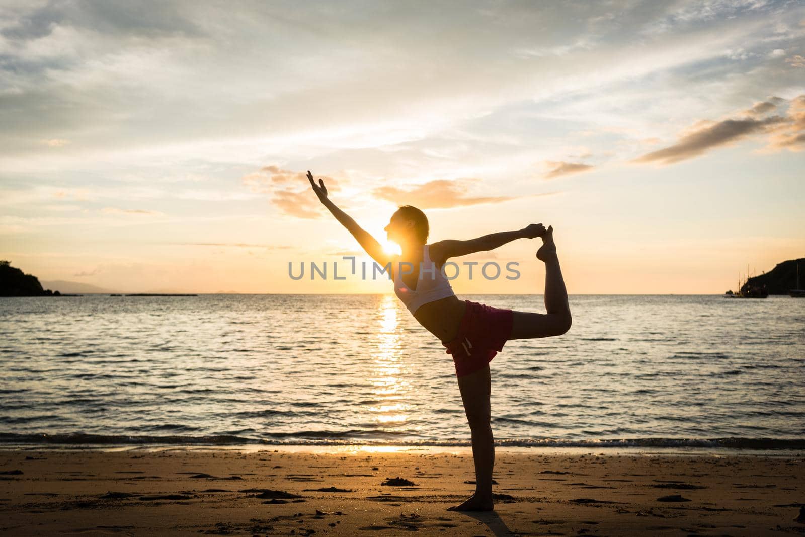 Fit woman practicing on the beach the standing bow pulling pose by Kzenon