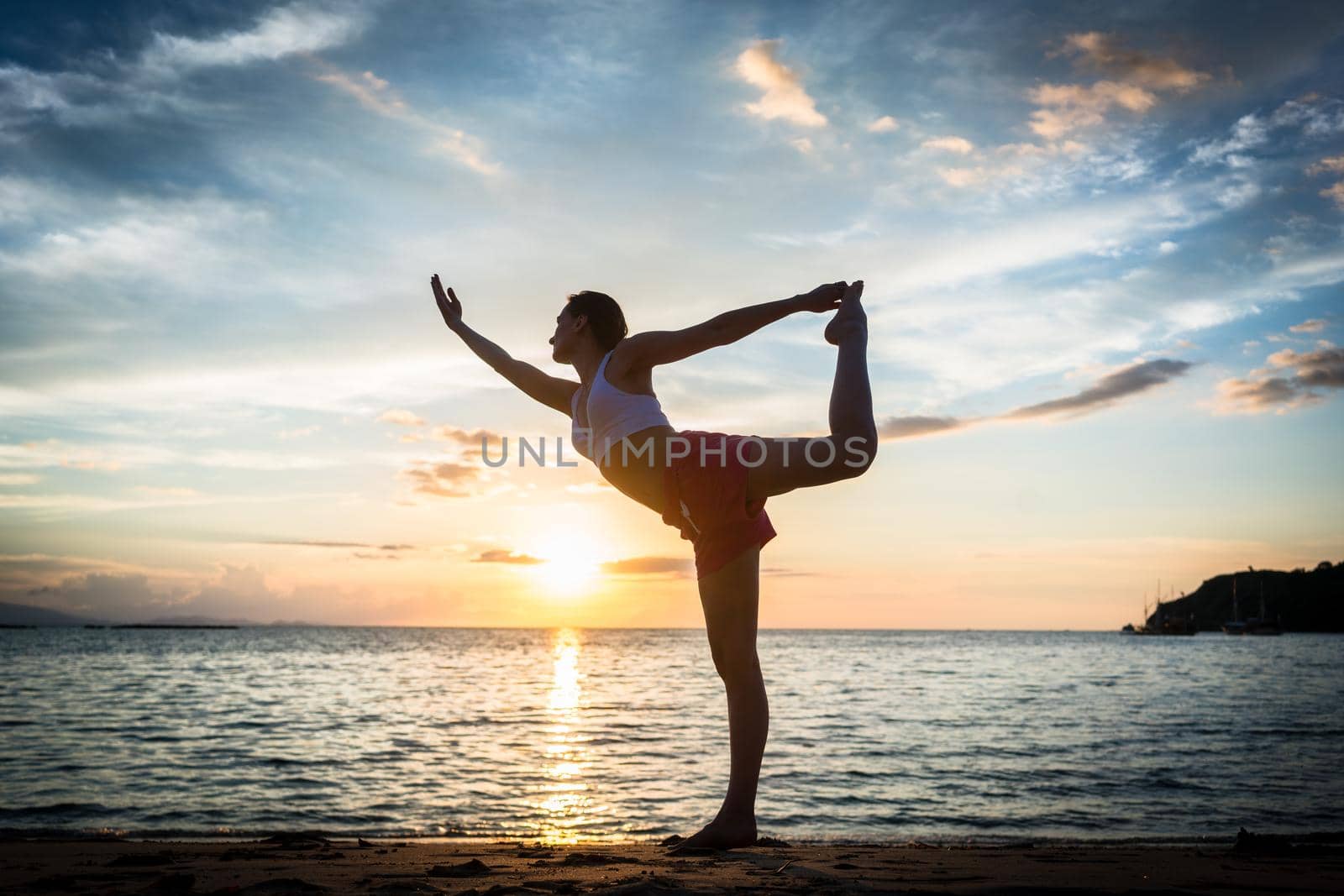 Fit woman practicing on the beach the standing bow pulling pose by Kzenon