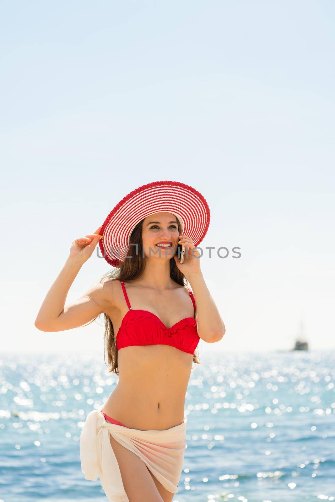 Fashionable fit young woman talking on mobile phone on the beach by Kzenon