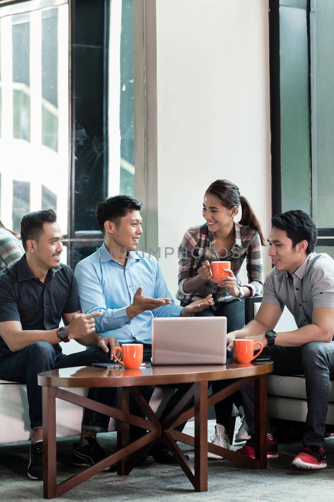 Team of four dedicated employees sitting in front of a laptop while working together at an innovative business project in a modern office