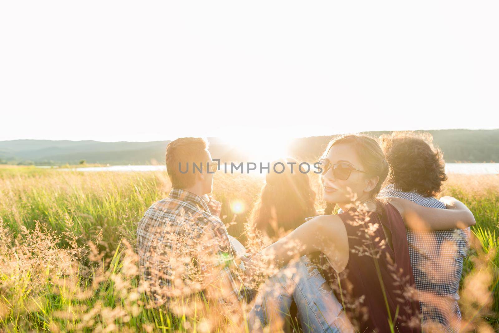 Friends sitting together at lake enjoying sunset by Kzenon