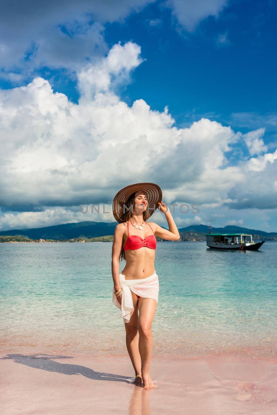 Fashionable young woman with a perfect body smiling while posing outdoors during summer vacation at Pink Beach, pink, in Komodo Island, Indonesia