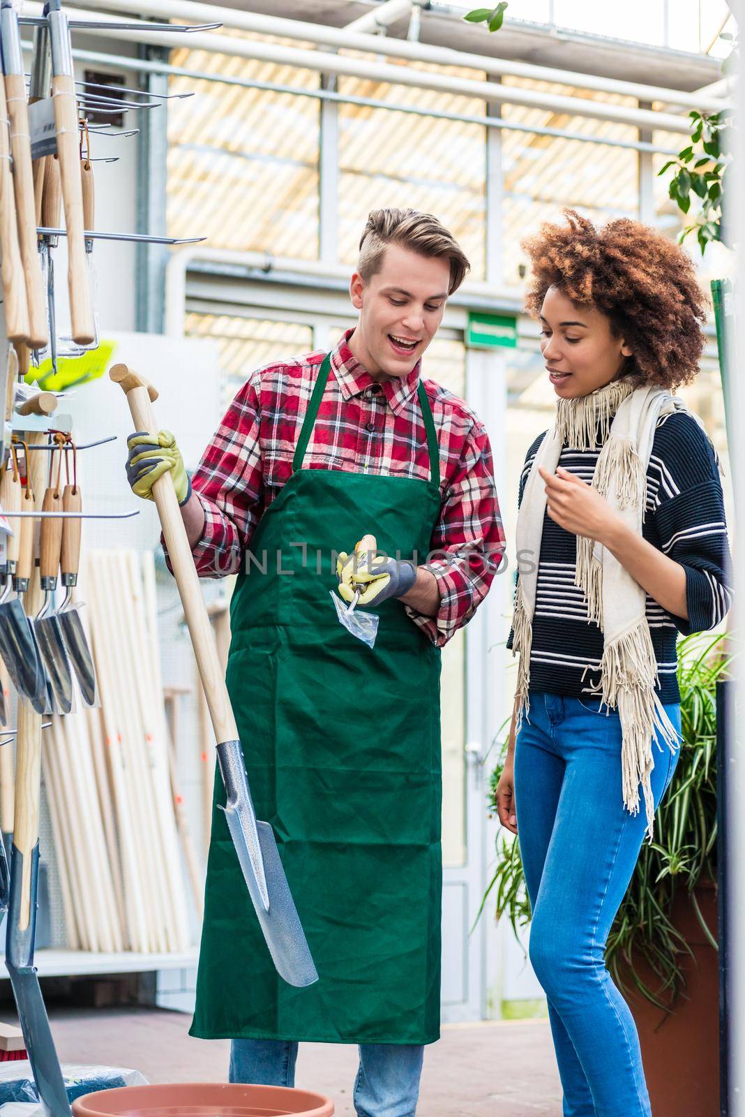 Handsome worker helping a customer with choosing a gardening tool by Kzenon