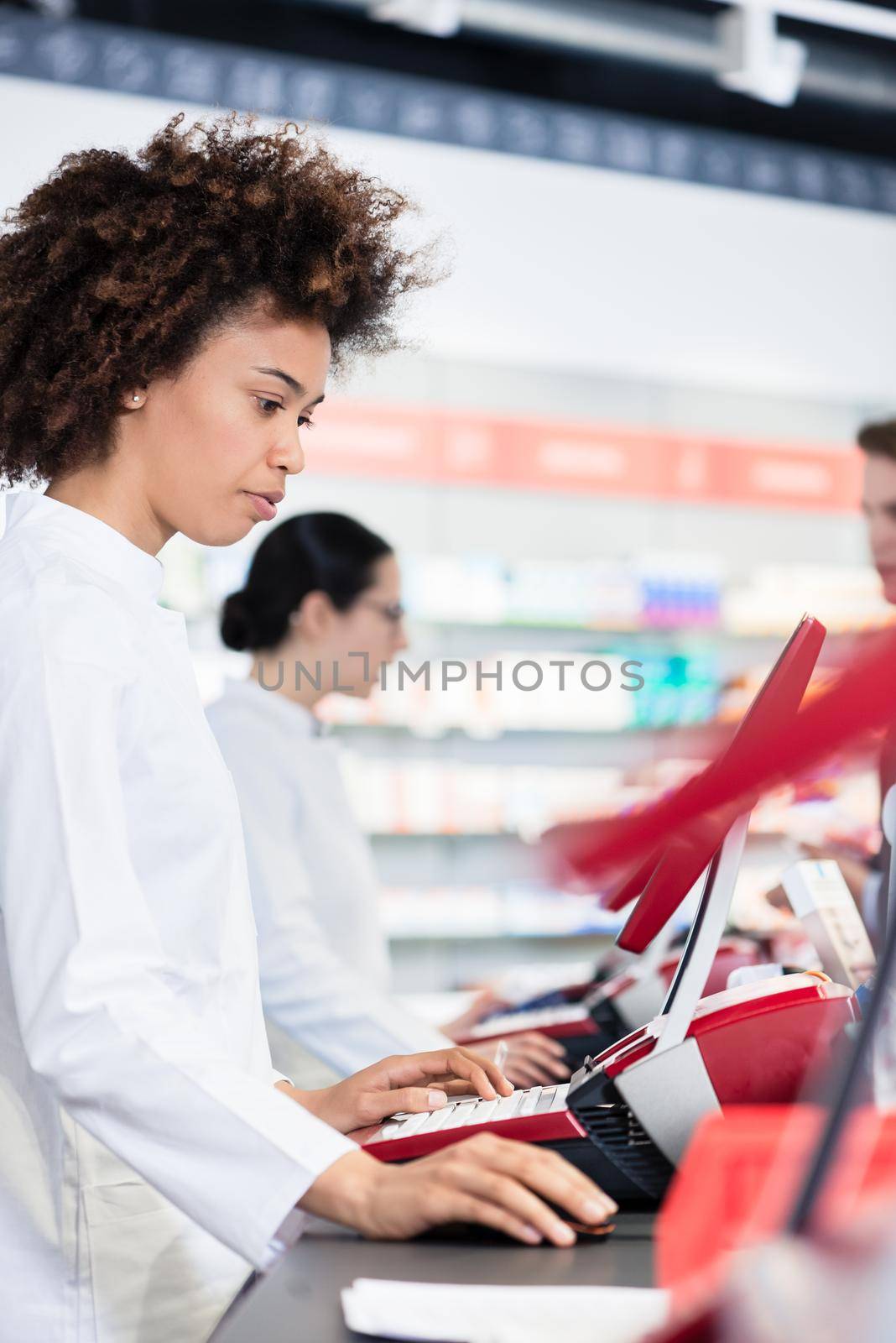 Side-view of a cheerful pharmacist holding two packs of prescribed medicine, while giving advices and useful information to a young male customer in a modern drugstore