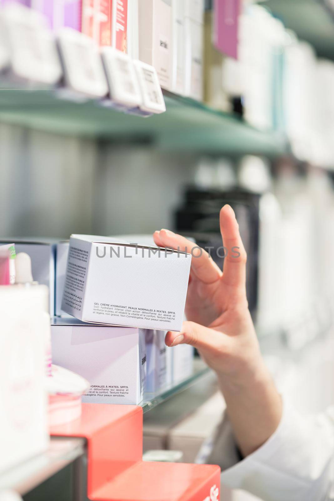 Close-up side view of the hand of a female pharmacist, picking up the package of the best pharmaceutical product from the shelf in a contemporary drugstore