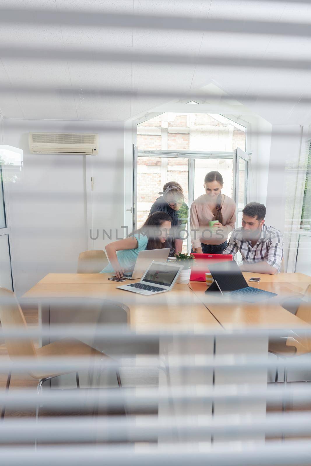 Close-up of the transparent interior window of an office with three young independent workers sharing the facilities of a modern co-working space
