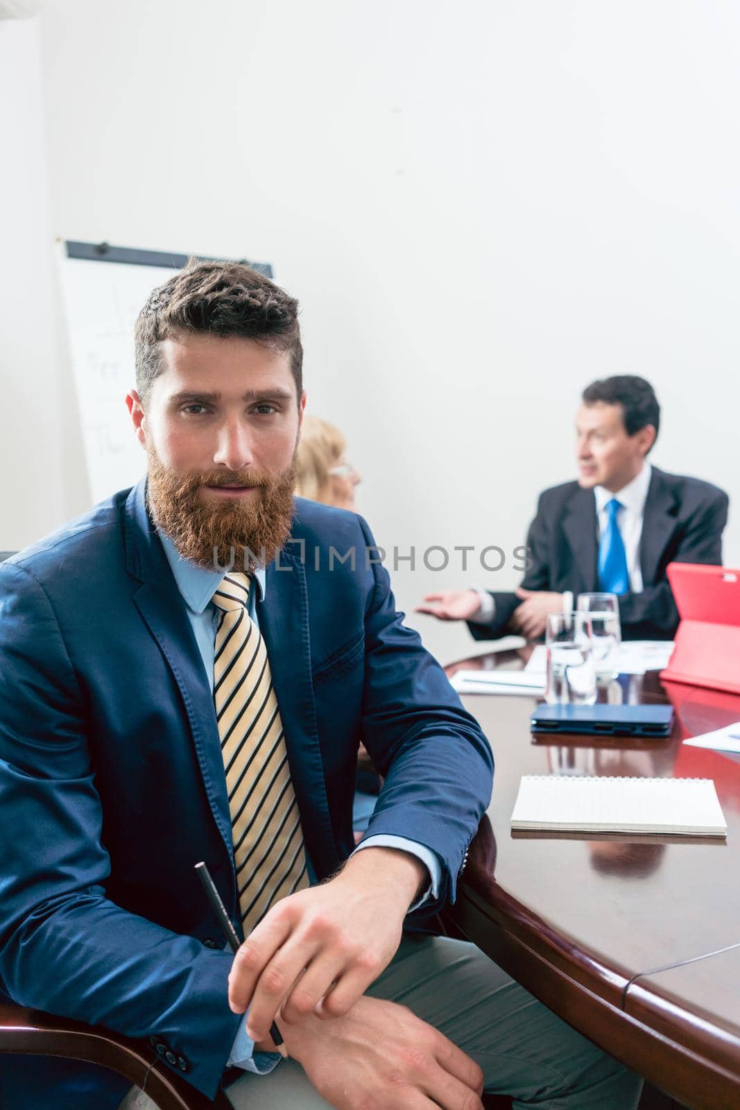 Portrait of a handsome young businessman wearing elegant formal suit, while looking at camera with confidence during a meeting in the conference room of a successful company