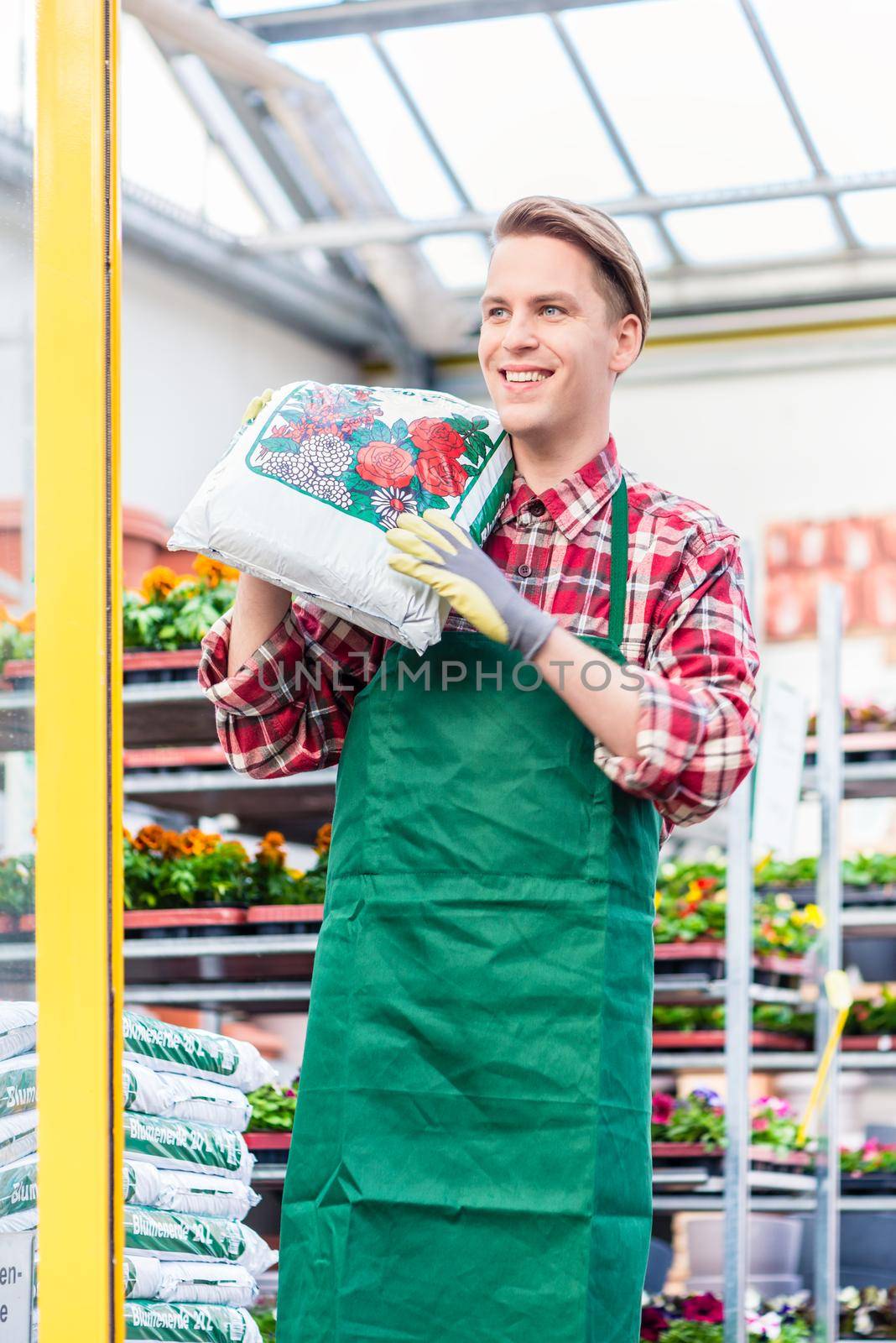 Cheerful young man carrying a bag of potting soil while working by Kzenon